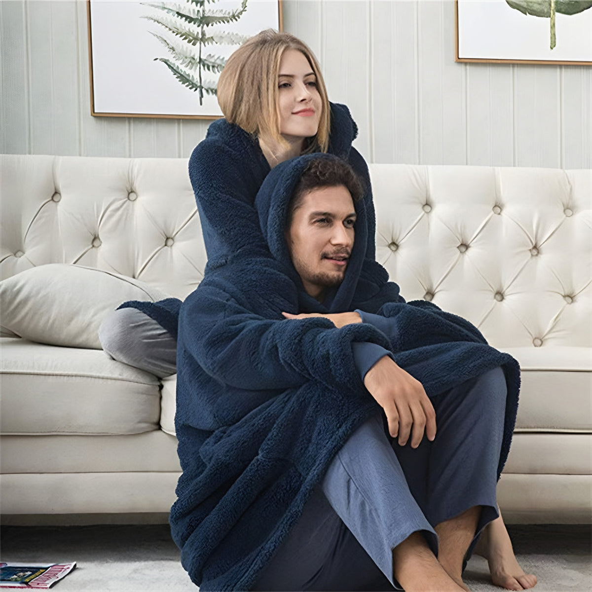 Couple cuddling on sofa wearing navy oversized blanket hoodies