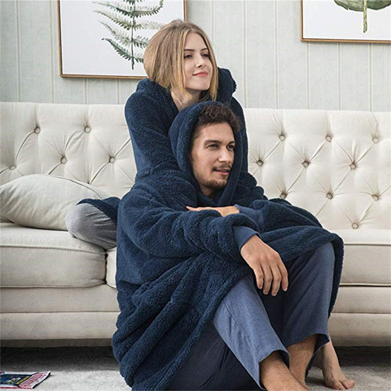 Couple cuddling on sofa wearing navy oversized blanket hoodies